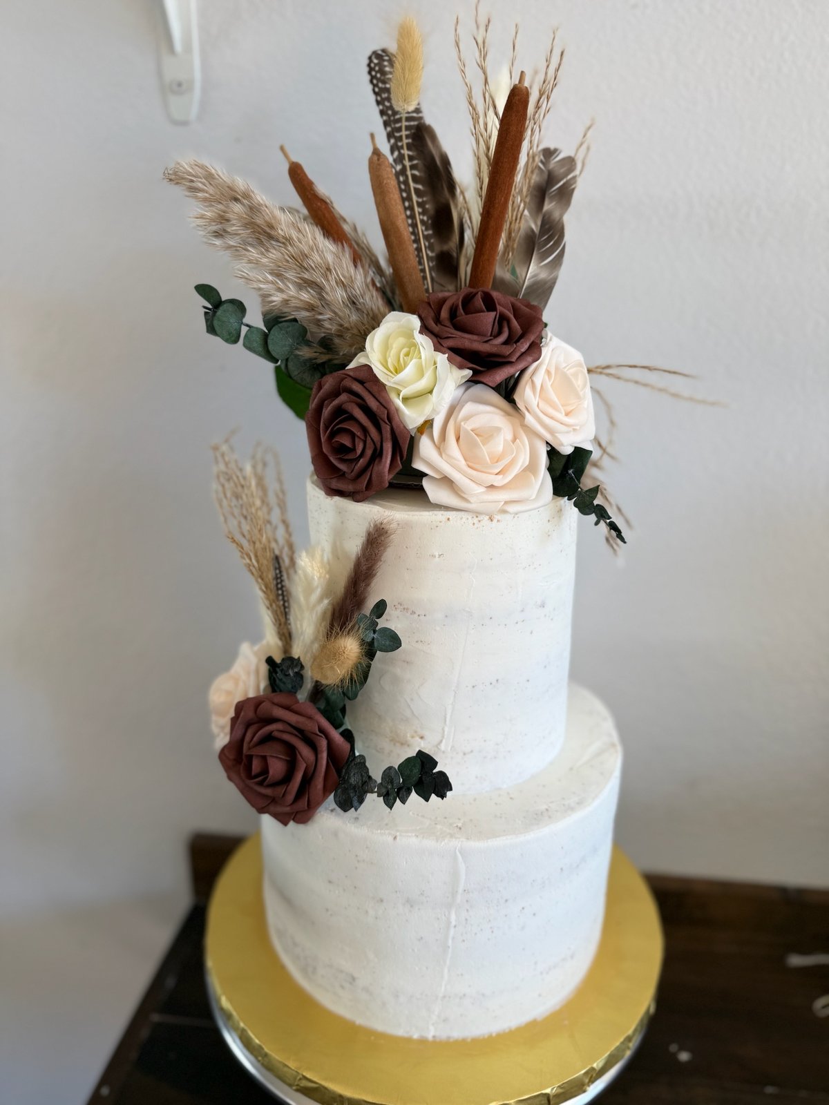 Two-tier ivory cake decorated with white and burgundy flowers and dried botanical stems